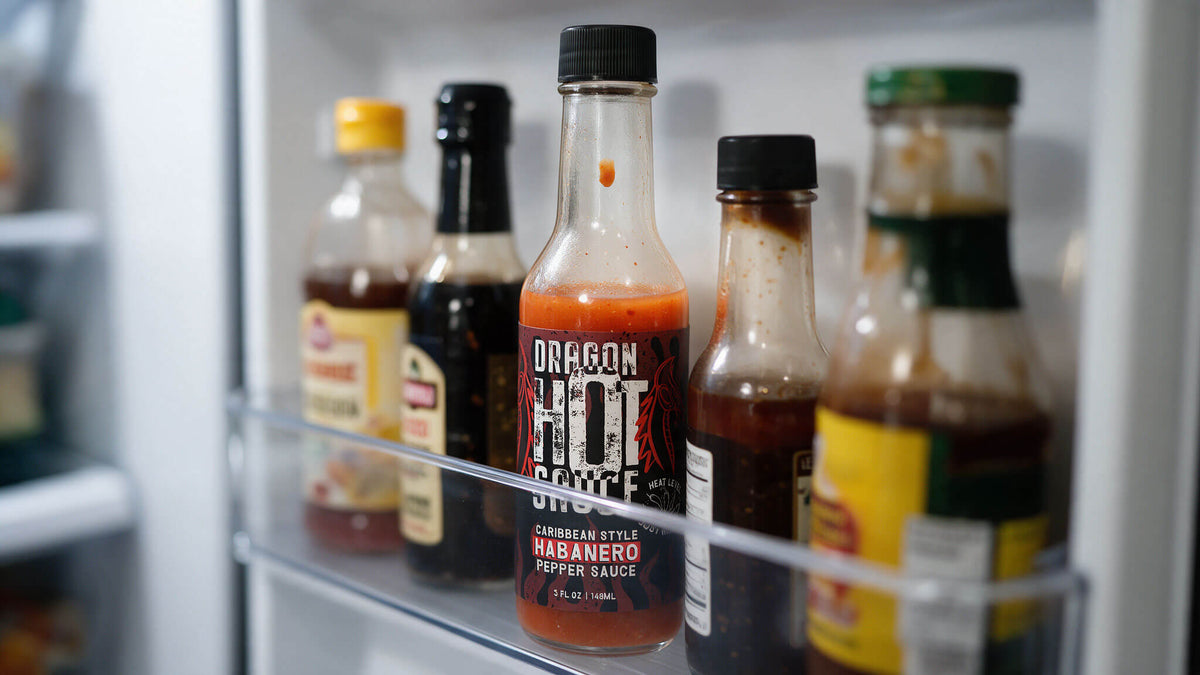 Opened bottle of Dragon Caribbean Style Habanero hot sauce with a drip on the neck, in a refrigerator door