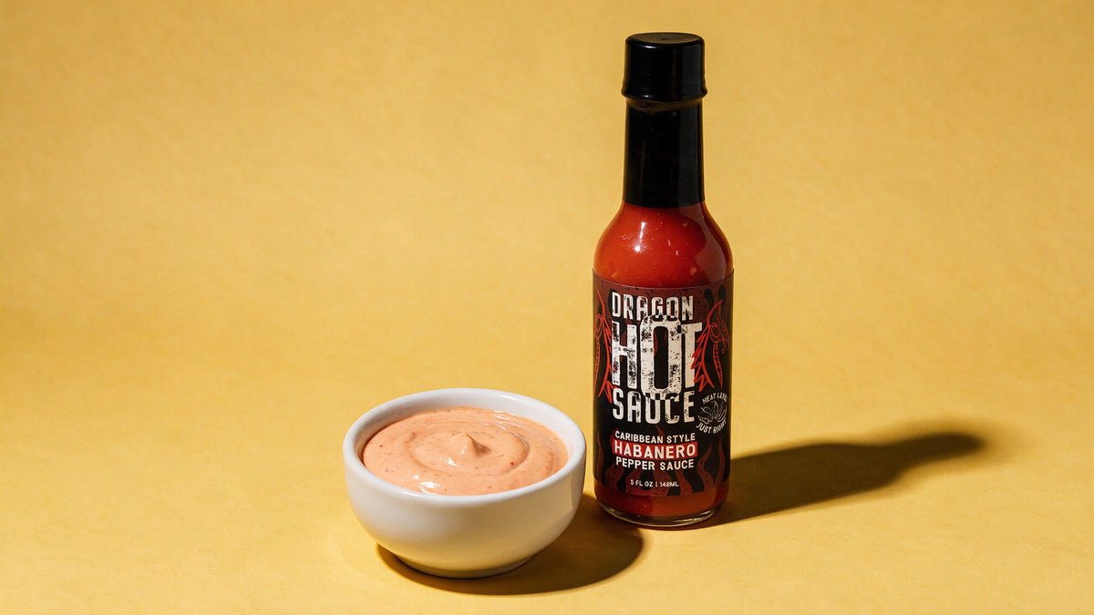 A small white bowl of creamy coral dragon sauce next to a bottle of Dragon Caribbean Style Habanero.