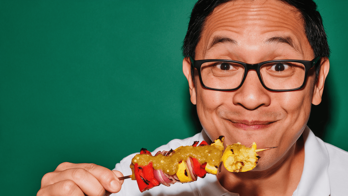 Man in glasses grinning behind a grilled vegetable kabob drizzled with green Fresh Serrano hot sauce
