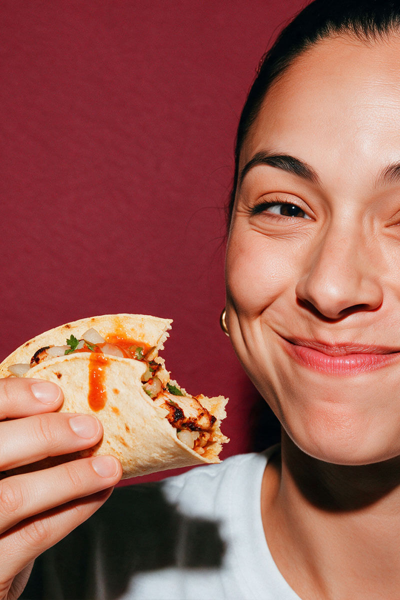 Young woman holding a soft taco topped with red Caribbean Style Habanero hot sauce